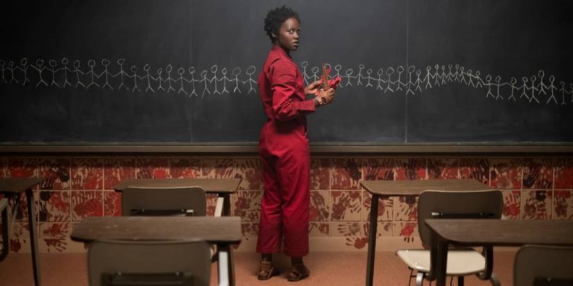 Lupita Nyong'o looking back infront of a blackboard in a dark classroom in "Us"
