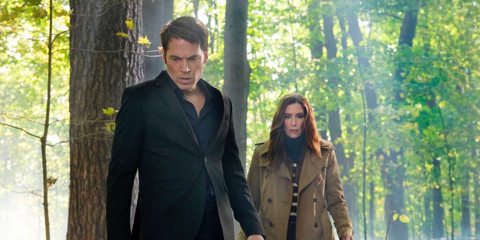 Tim Rozon and Sarah Levy look down at the ground with concern in the woods in SurrealEstate