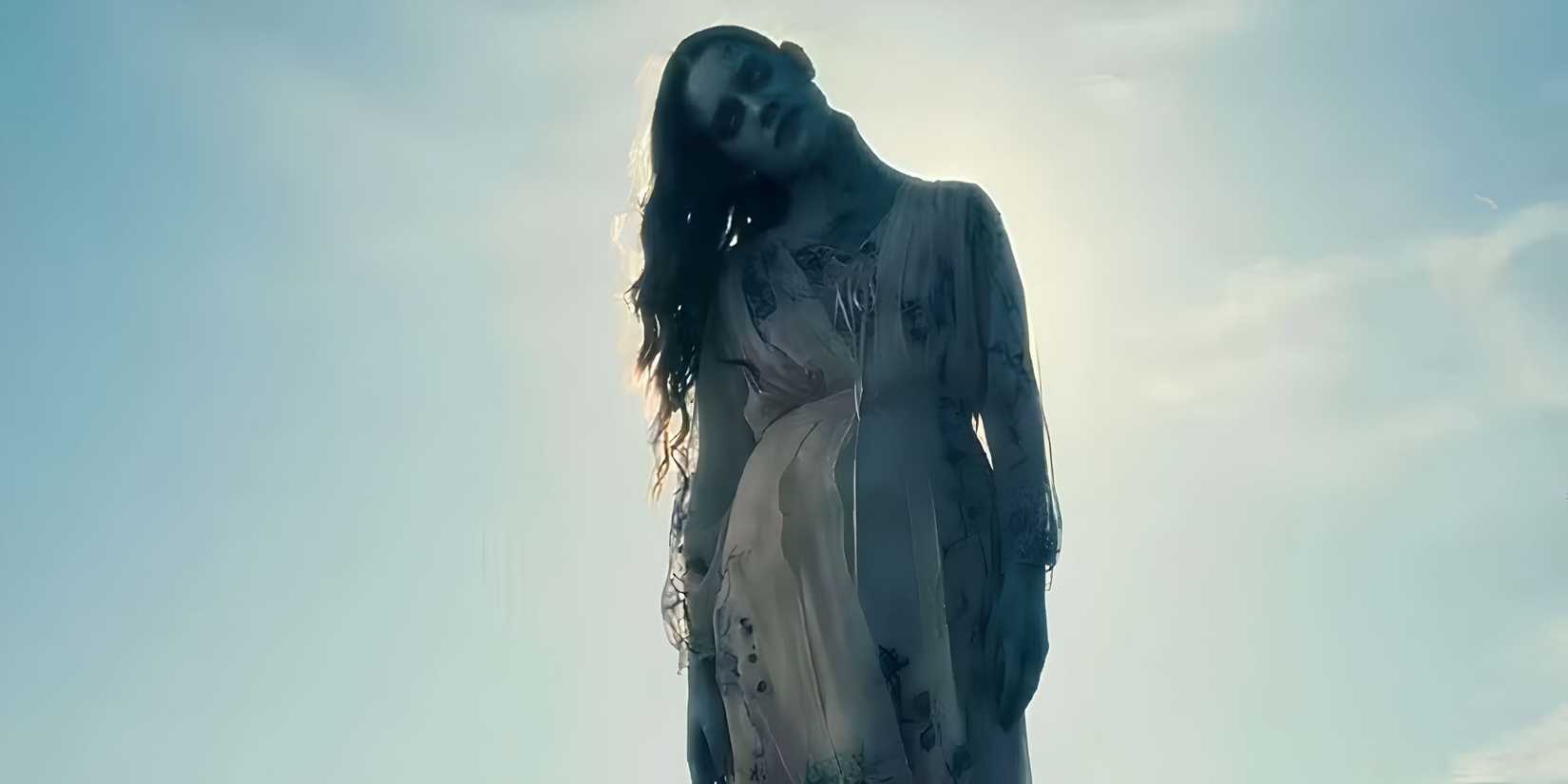The Bent-Neck Lady (Victoria Pedretti) seen standing outside under blue skies in The Haunting of Hill House.