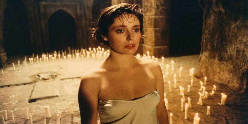 A woman standing still with many candles on the floor behind her in The-Church