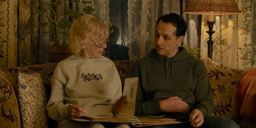 Ruth flipping through an album on the couch while talking to Tom in Widow's Bay.