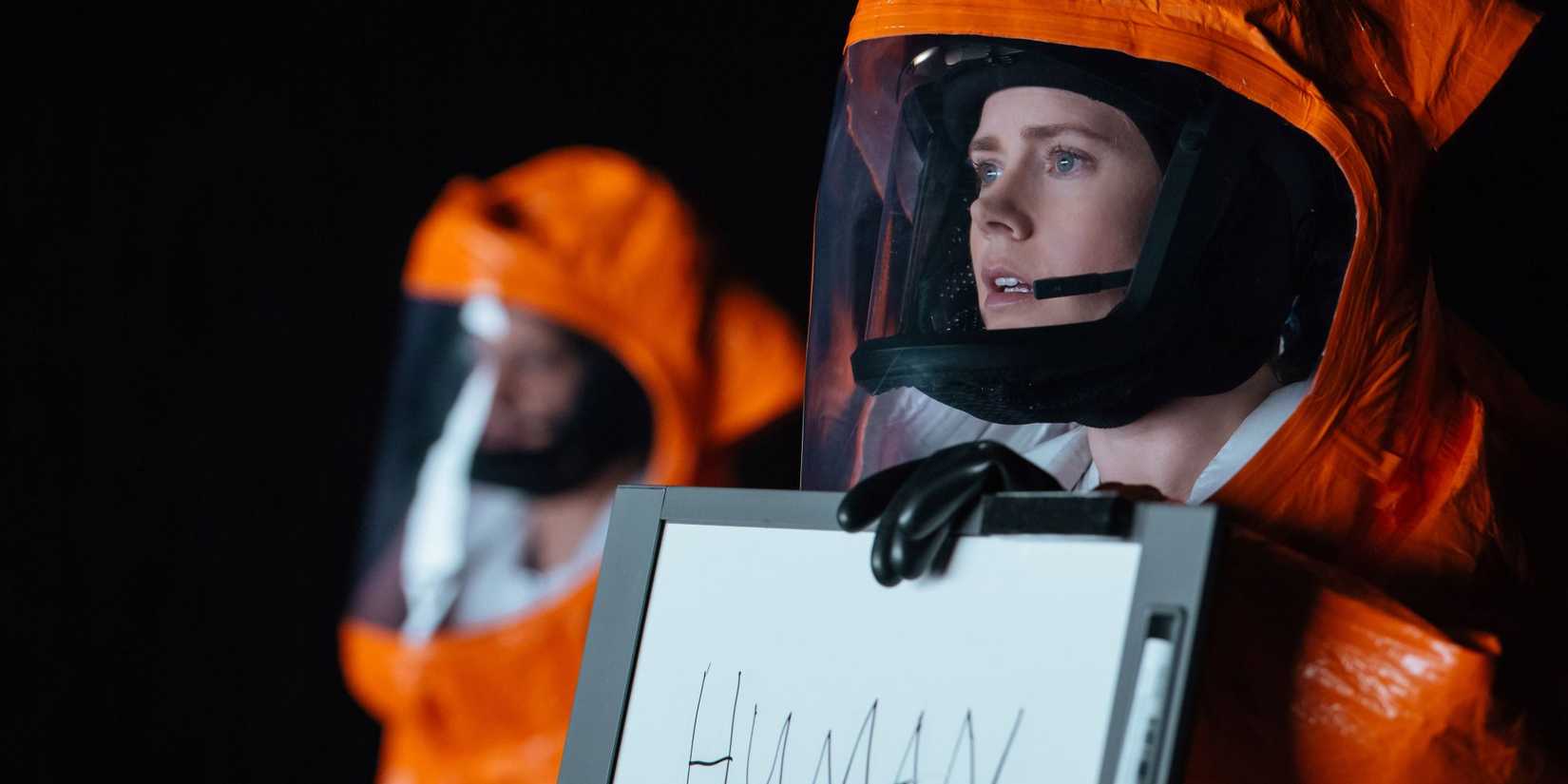 Amy Adams as Louise holding a dry erase board that says "human" and wearing a hazmat suit in Arrival