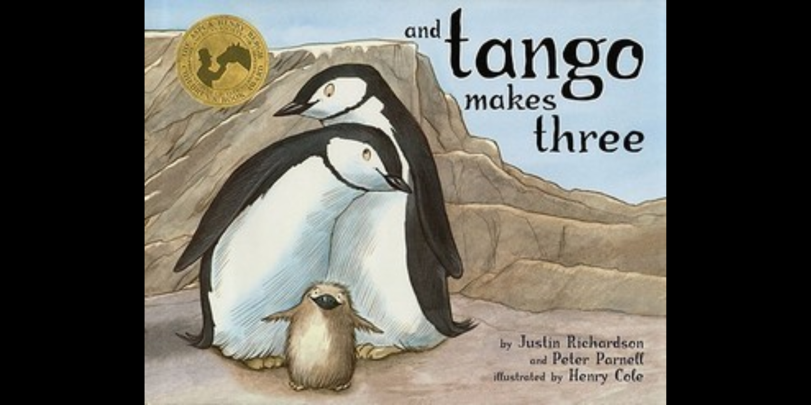 Book cover of And Tango Makes Three, showing two adult penguins standing together behind a baby penguin against a rocky backdrop. The title appears in large black text on a light blue sky.