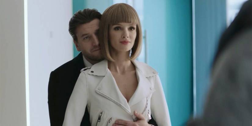 A man hugging a robotic looking woman from behind as they stare in the mirror in Better Than Us.