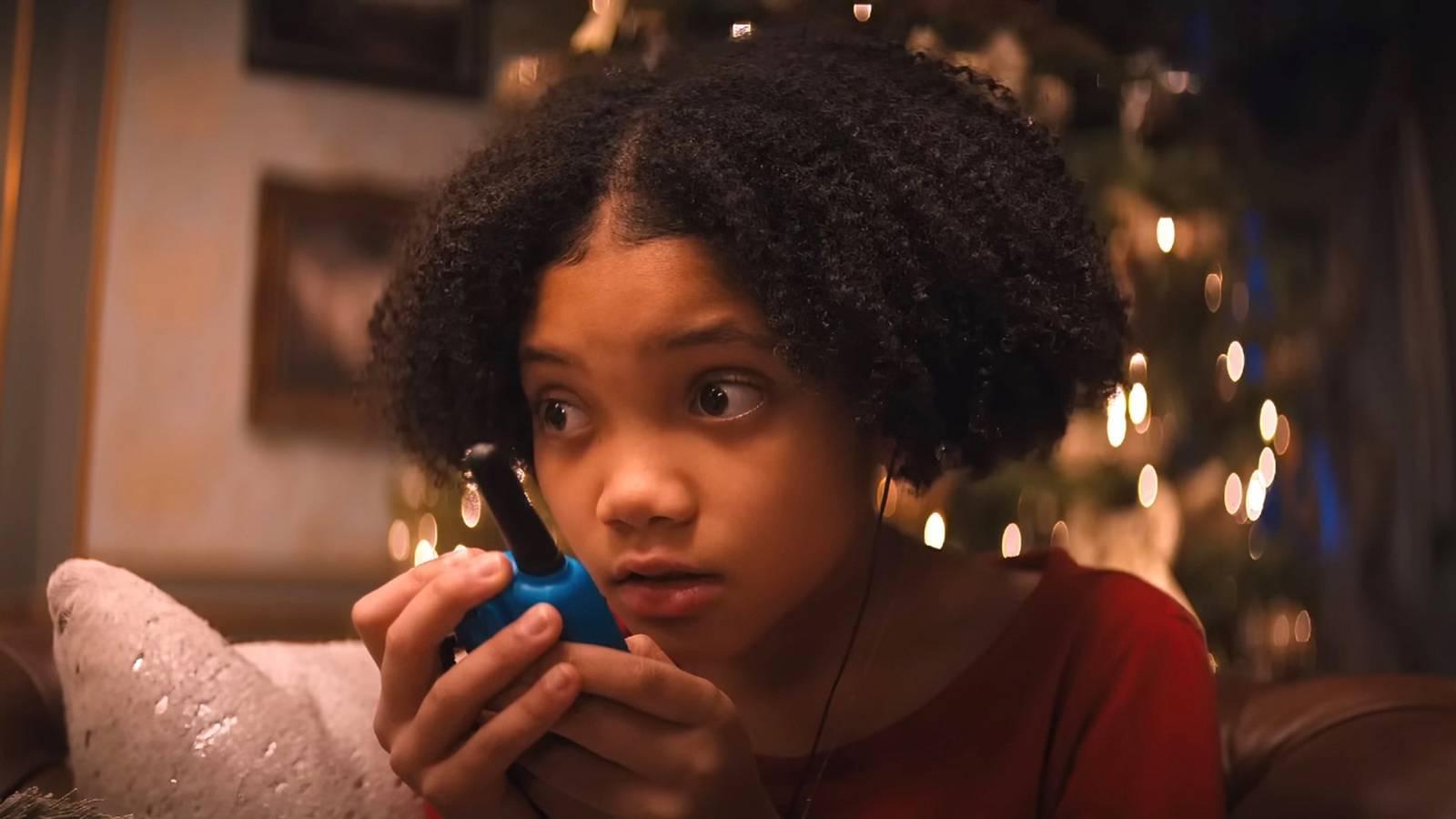 Leah Brady talking into a walkie talkie with a Christmas tree behind her - Violent Night