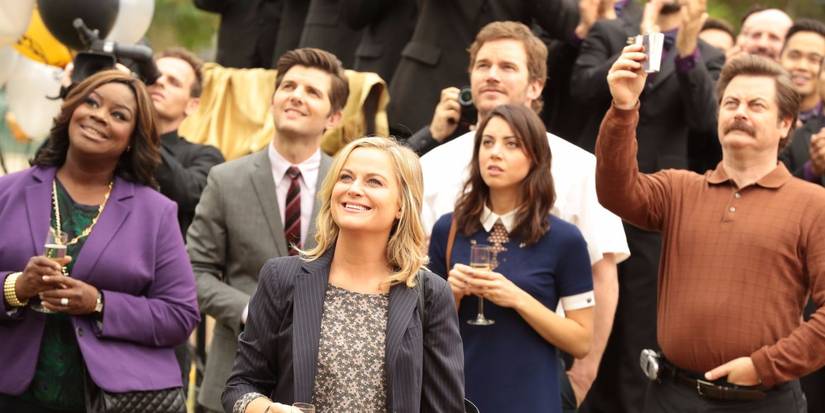 The cast of Parks and Recreation holding champagne and toasting