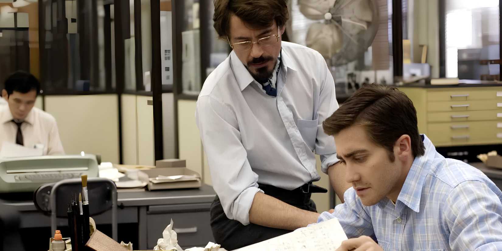 Paul Avery (Robert Downey Jr.) looks over Robert Graysmith (Jake Gyllenhaal) at his desk in Zodiac.
