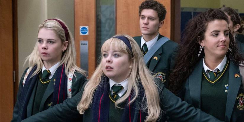 Nicola Coughlan as Clare Devlin stands in front of her friends with arms out, looking anxious on Derry Girls