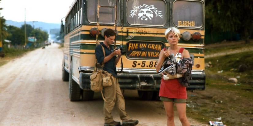 Scoot McNairy and Whitney Able stand behind an old school bus on a dirt road in Monsters