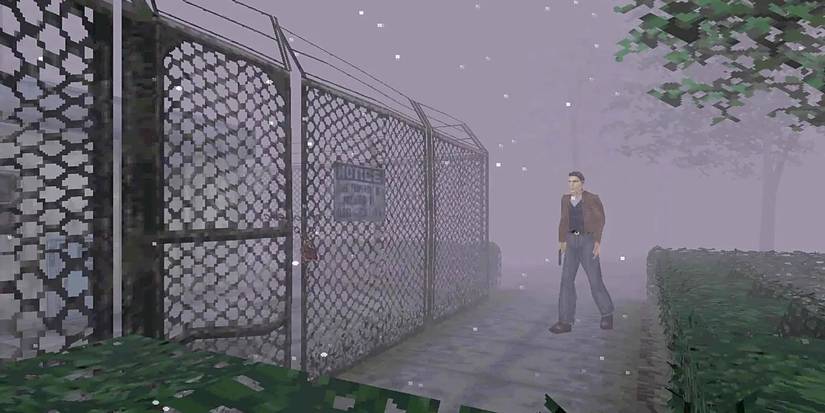 A man walking up to a gated fence in an area overwhelming with fog in 'Silent Hill' (1999) on the PlayStation.