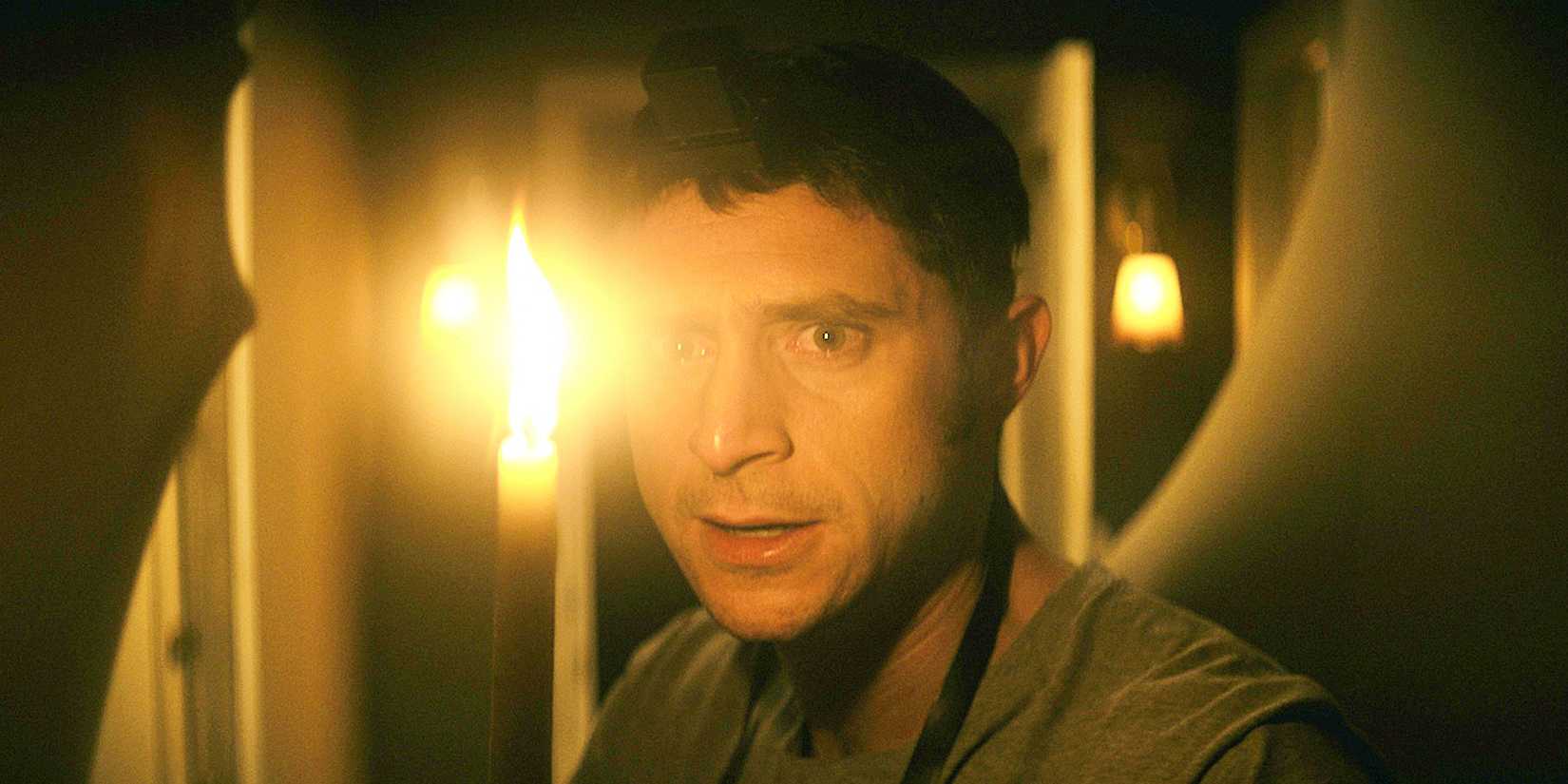 A man with a candle looking scared in the-vigil