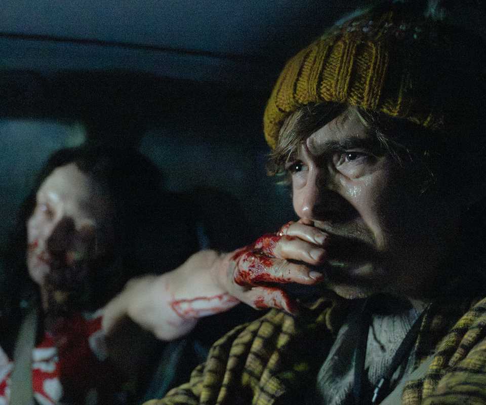 A zombie woman holding her bloodied hand in front of Austin Abrams' mouth in Resident Evil