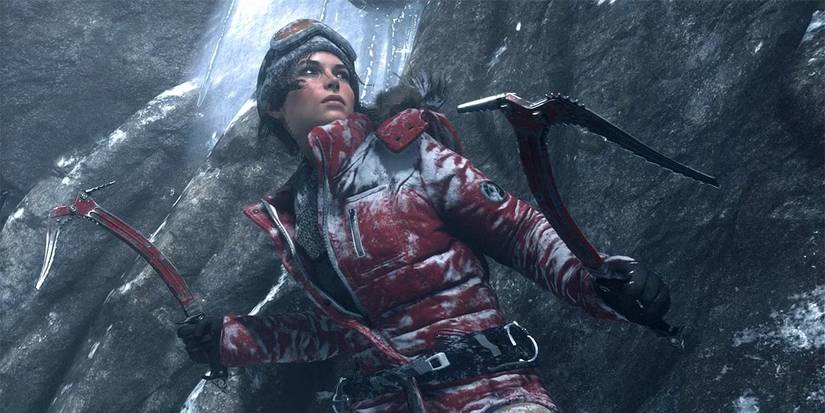 Lara Croft climbing a snowy cliff with red ice axes in Rise of the Tomb Raider