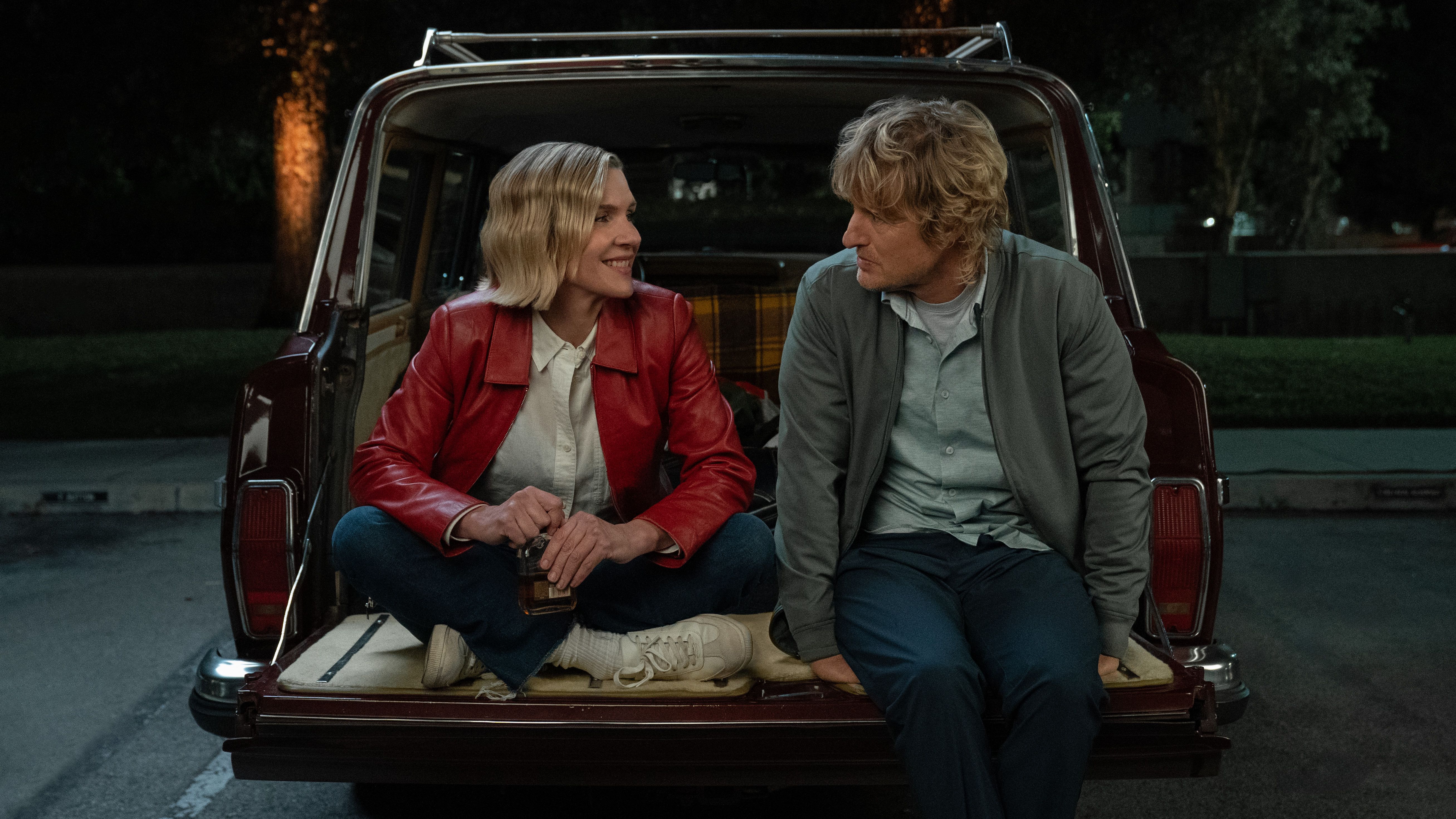 Rhea Seehorn sitting with Owen Wilson in the open back of a car in Stick Season 2