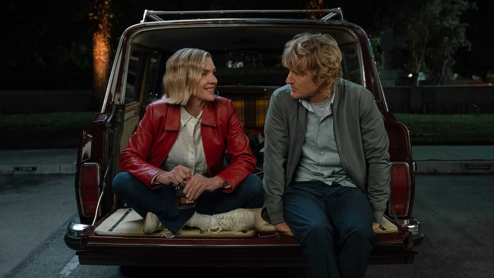 Rhea Seehorn sitting with Owen Wilson in the open back of a car in Stick Season 2