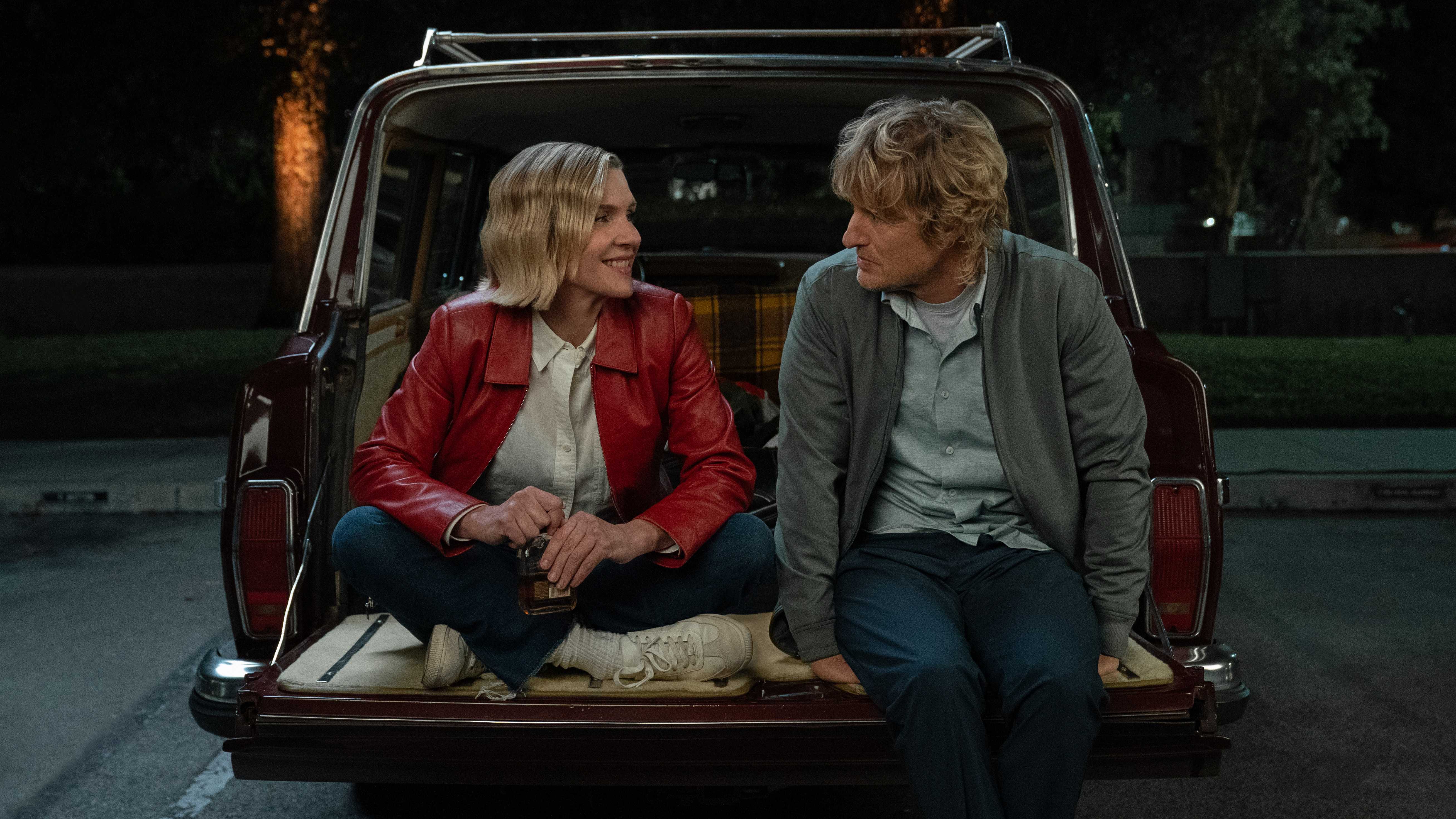 Rhea Seehorn sitting with Owen Wilson in the open back of a car in Stick Season 2