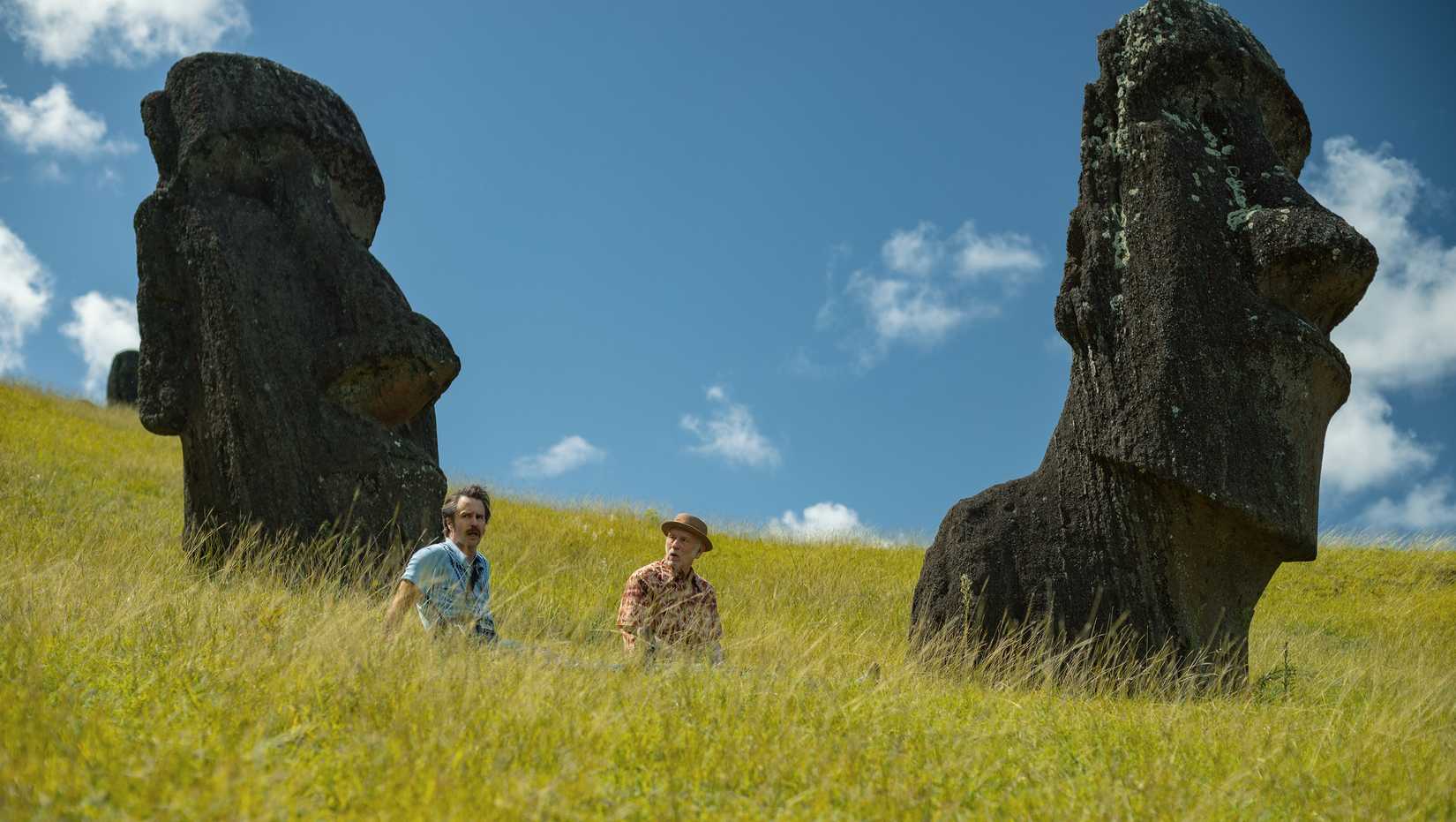 Sam Rockwell and John Malkovich standing in waves of grass between Easter Island statues in Wild Horse Nine