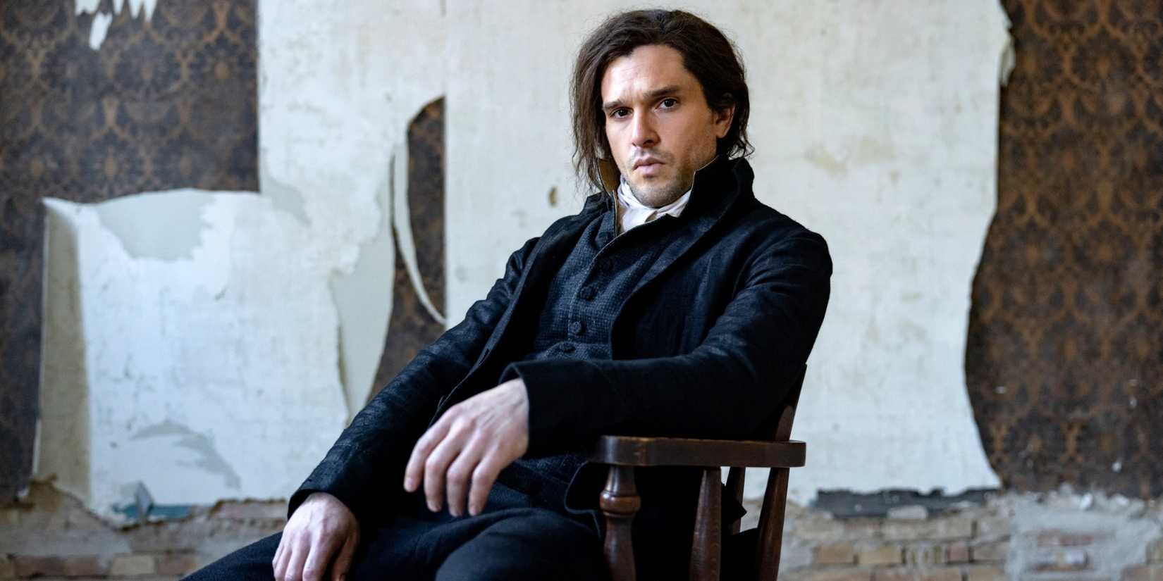 Kit Harington as Sydney Carton sitting on a chair in an empty decaying room in A Tale of Two Cities