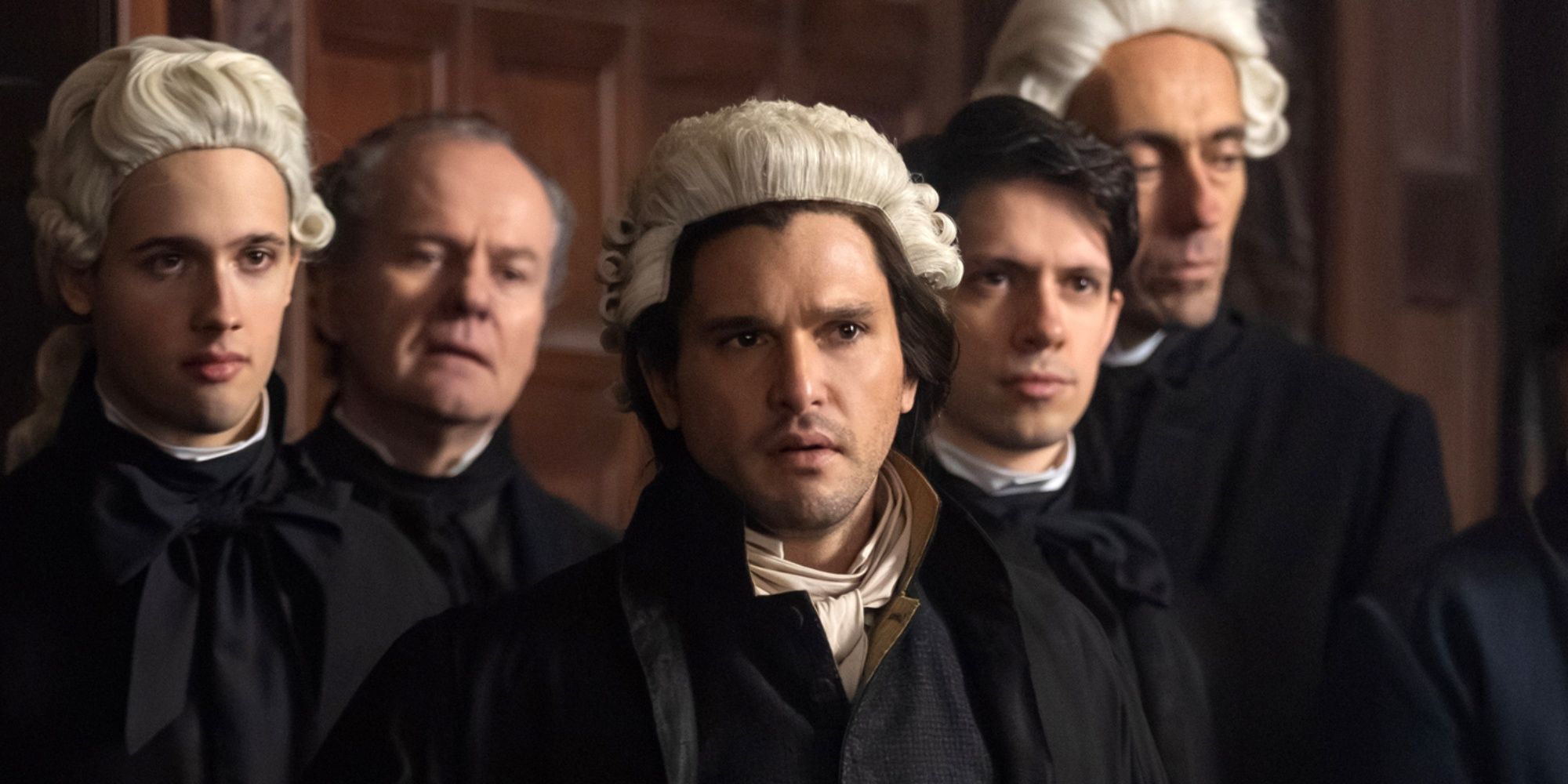 Kit Harington as Sydney Carton standing in a courtroom surrounded by lawyers in A Tale of Two Cities