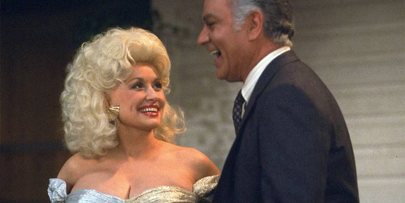 Dolly Parton in a metallic dress smiling next to a laughing man in a suit