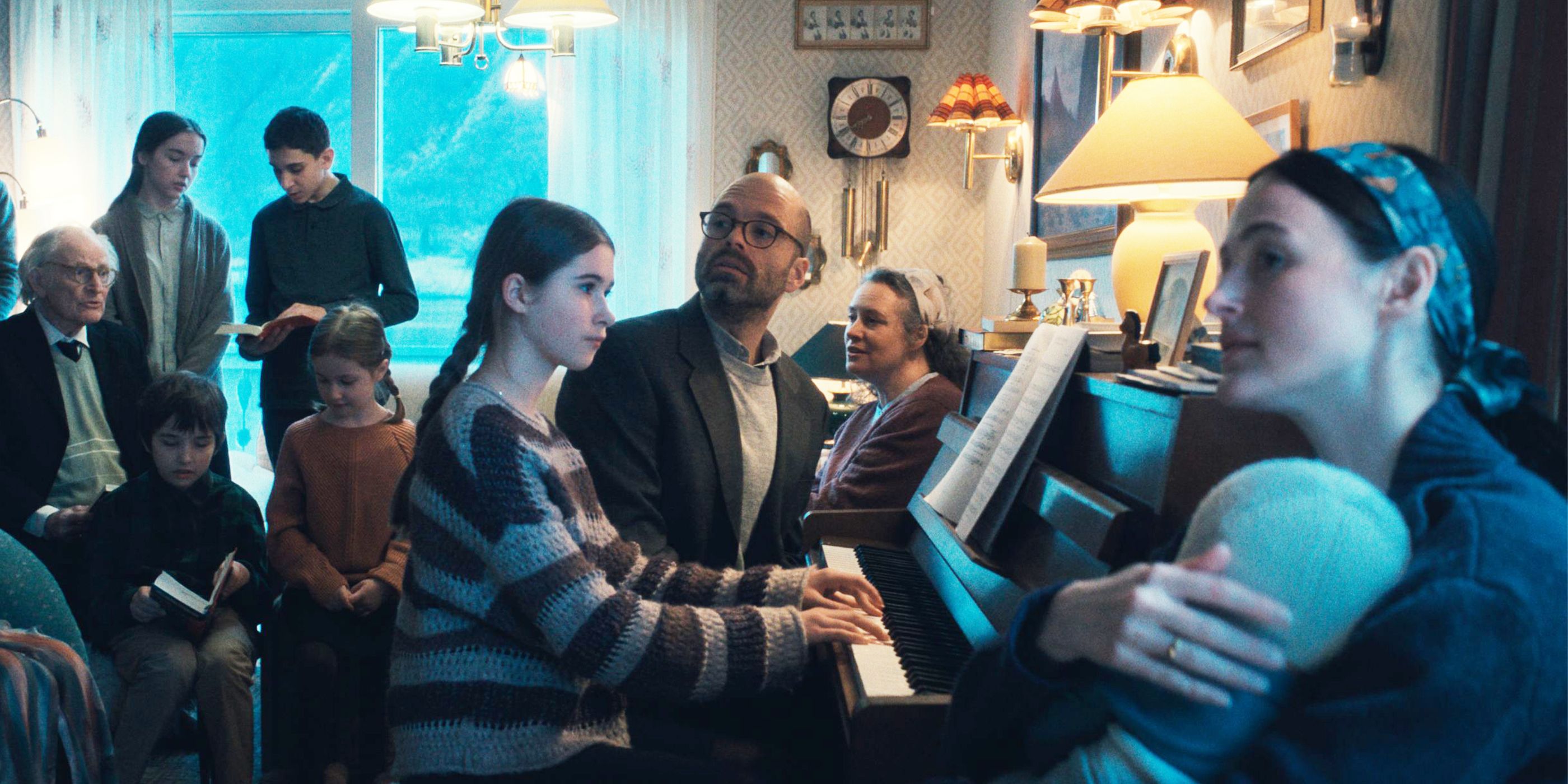 A little girl and her father play piano in a room full of people.