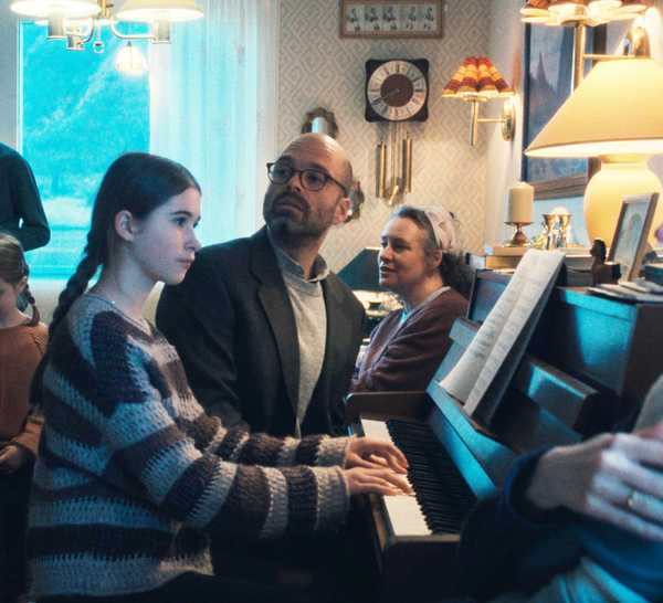 A little girl and her father play piano in a room full of people.