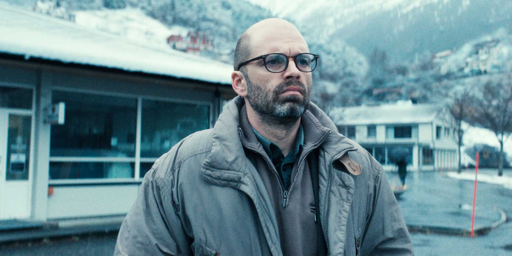 A man stands outside in the cold in a jacket and glasses.