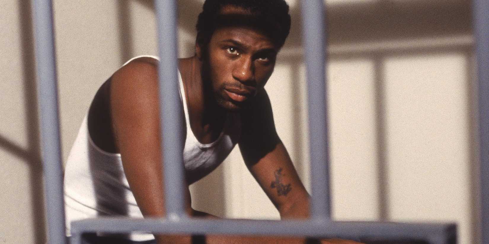 Leon wearing a wifebeater, sitting in his prison cell bed, in 'Capital P' from 'Oz'