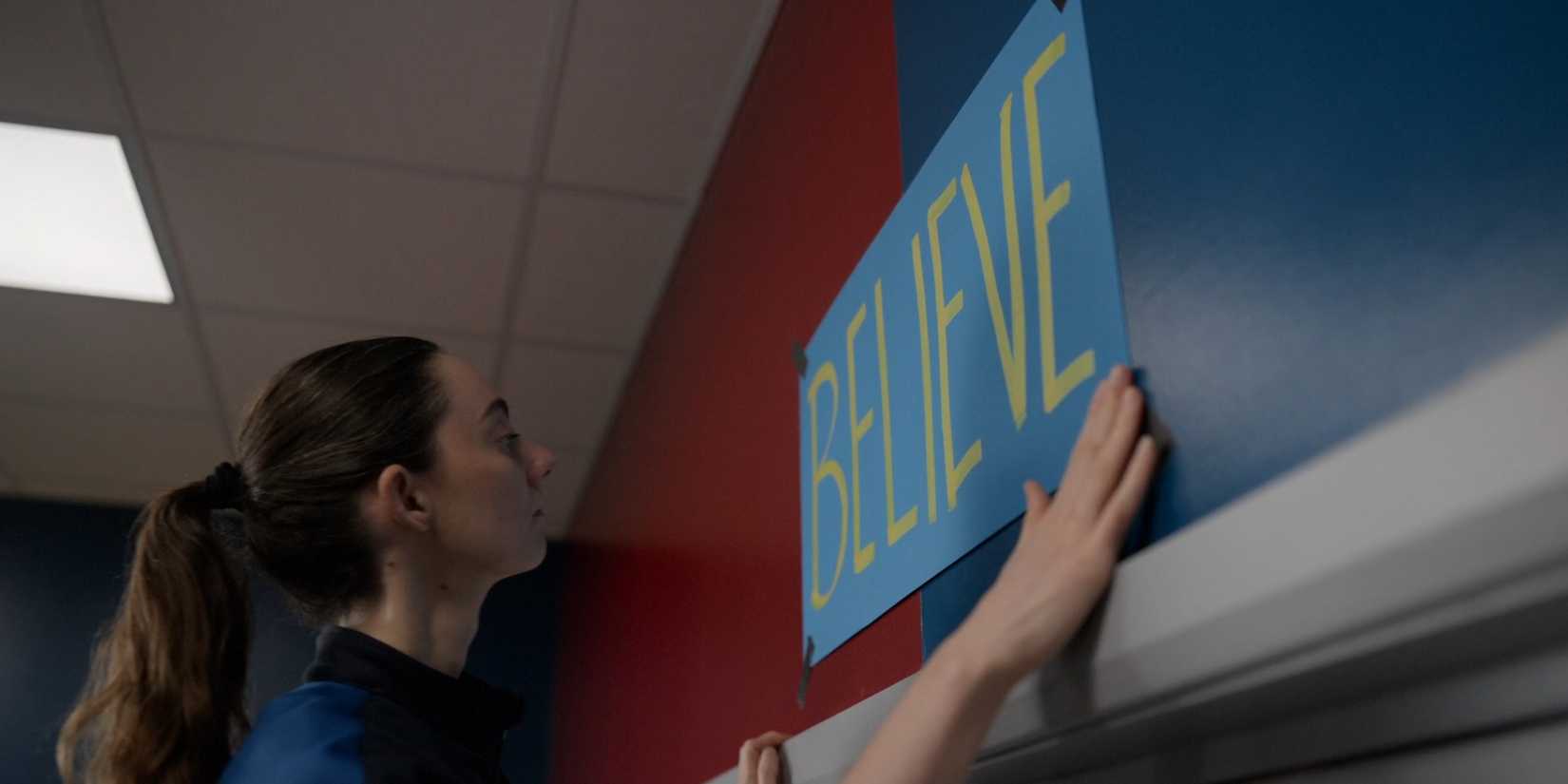 Tanya Reynolds putting up a blue sign saying "Believe" on a wall in Ted Lasso