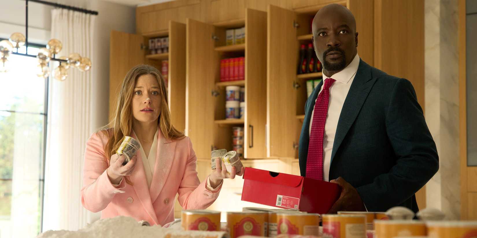 Mike Colter as Michael Price standing with Rachel Keller as Olivia Siffre holding money rolls in Cupertino