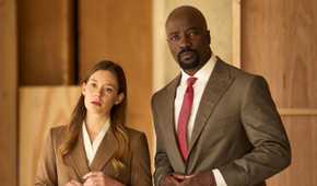 Mike Colter as Michael Price standing next to Rachel Keller as Olivia Siffre in their office in Cupertino