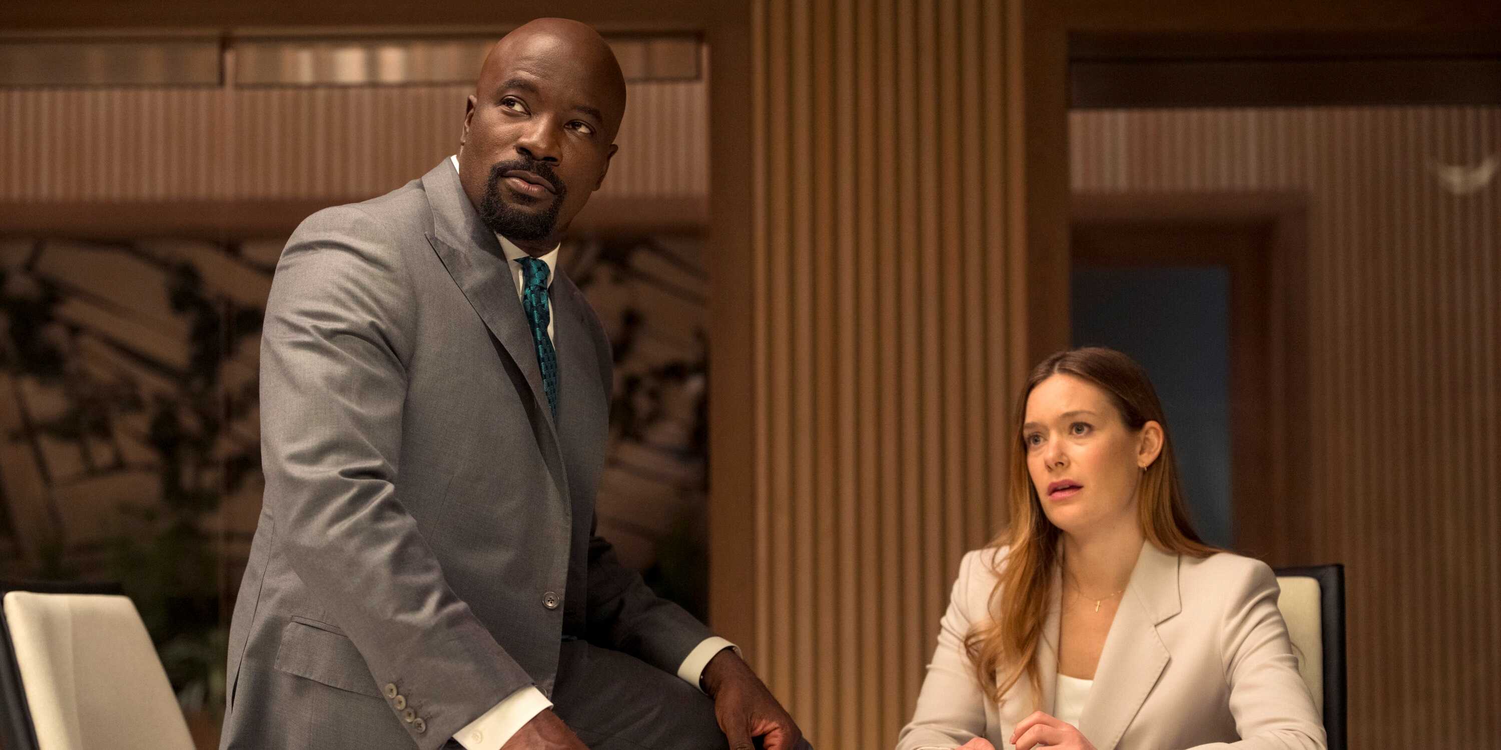 Mike Colter as Michael Price sitting on a table next to Rachel Keller as Olivia Siffre in Cupertino