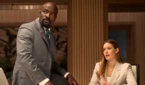 Mike Colter as Michael Price sitting on a table next to Rachel Keller as Olivia Siffre in Cupertino