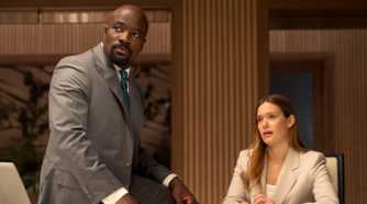 Mike Colter as Michael Price sitting on a table next to Rachel Keller as Olivia Siffre in Cupertino