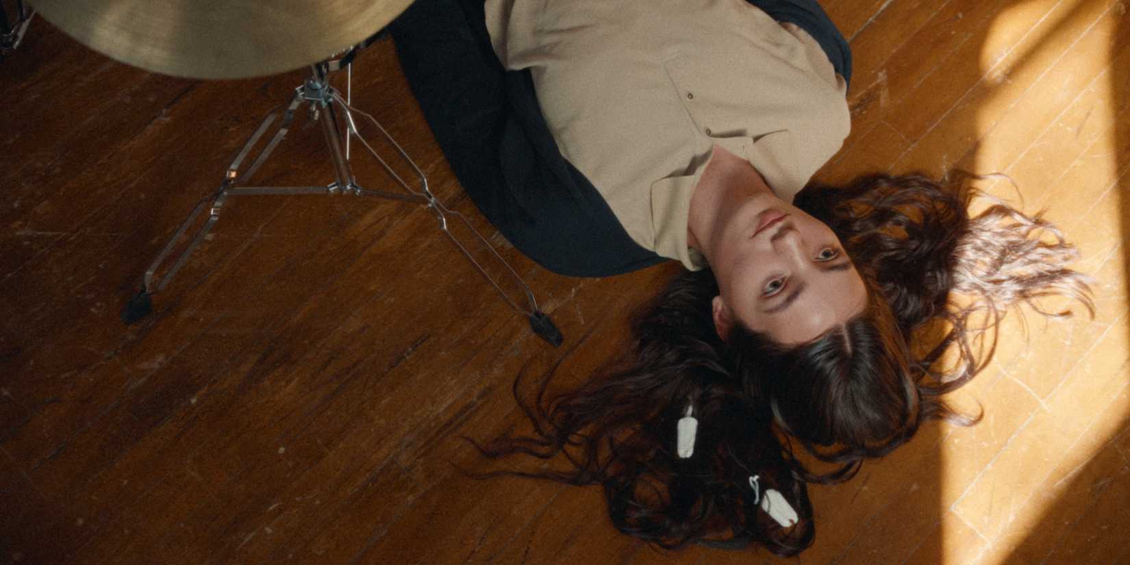 Adi Madden Cabrera as Edie lying on the wood floor next to part of her drum set in Edie Arnold is a Loser