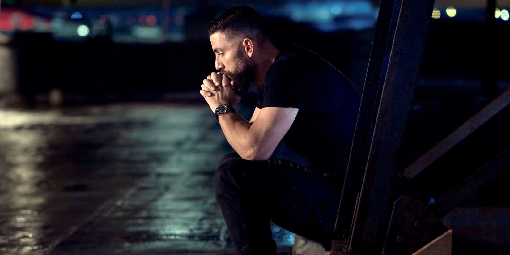 Zeeko Zaki as OA sitting outside with his elbows resting on his knees in FBI Season 9