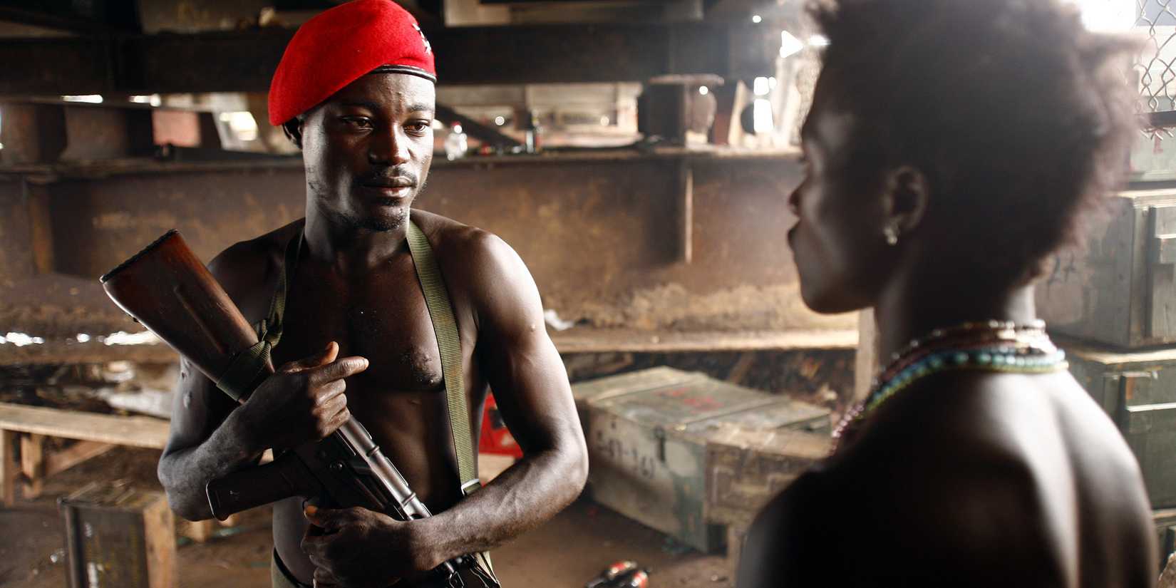 Man with gun and red beret looking at young man in 'Johnny Mad Dog'