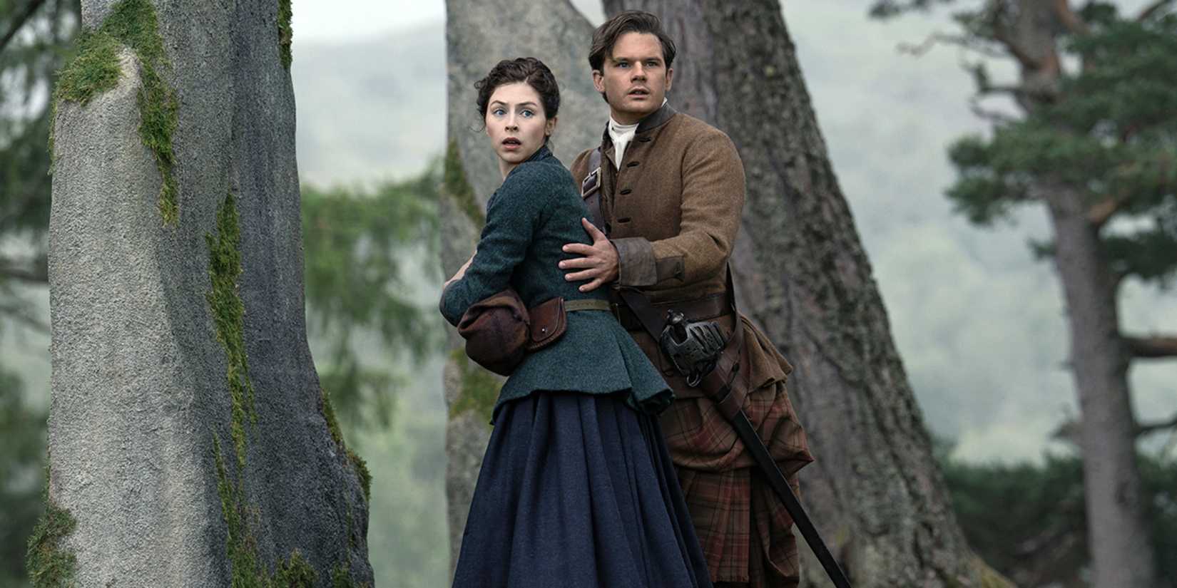 Jeremy Irvine as Henry holding Hermione Corfield as Julia in Outlander: Blood of My Blood Season 2