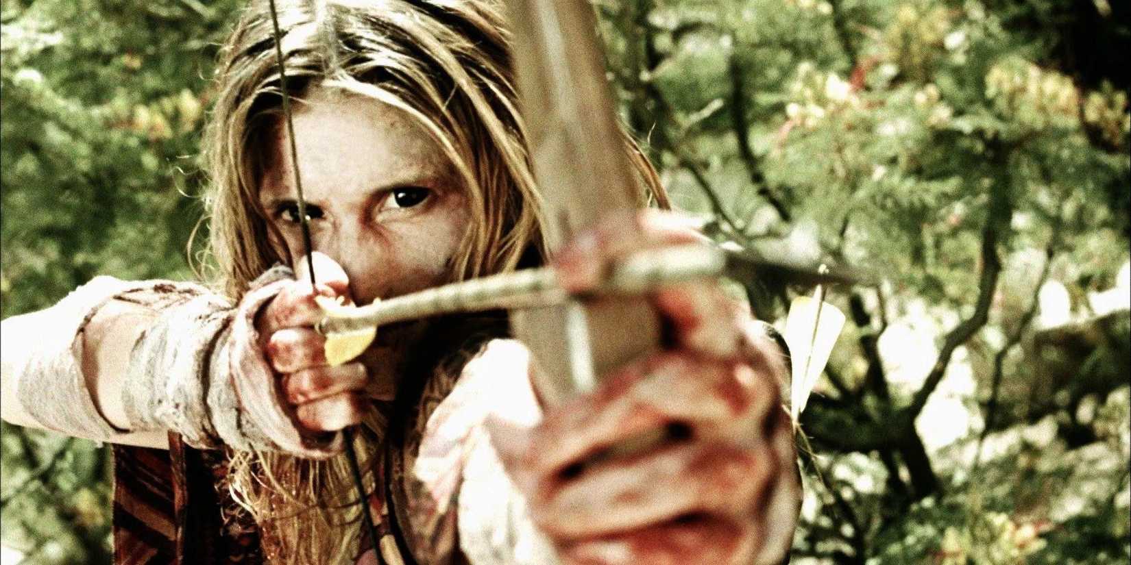 Amanda Adrienne as Zoe aiming a bow and arrow in the middle of the forest in 'Savaged'