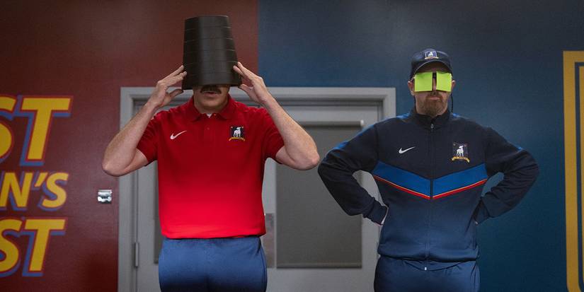 Ted with a bucket on his head, Coach Beard with sticky notes over his eyes in Ted Lasso.