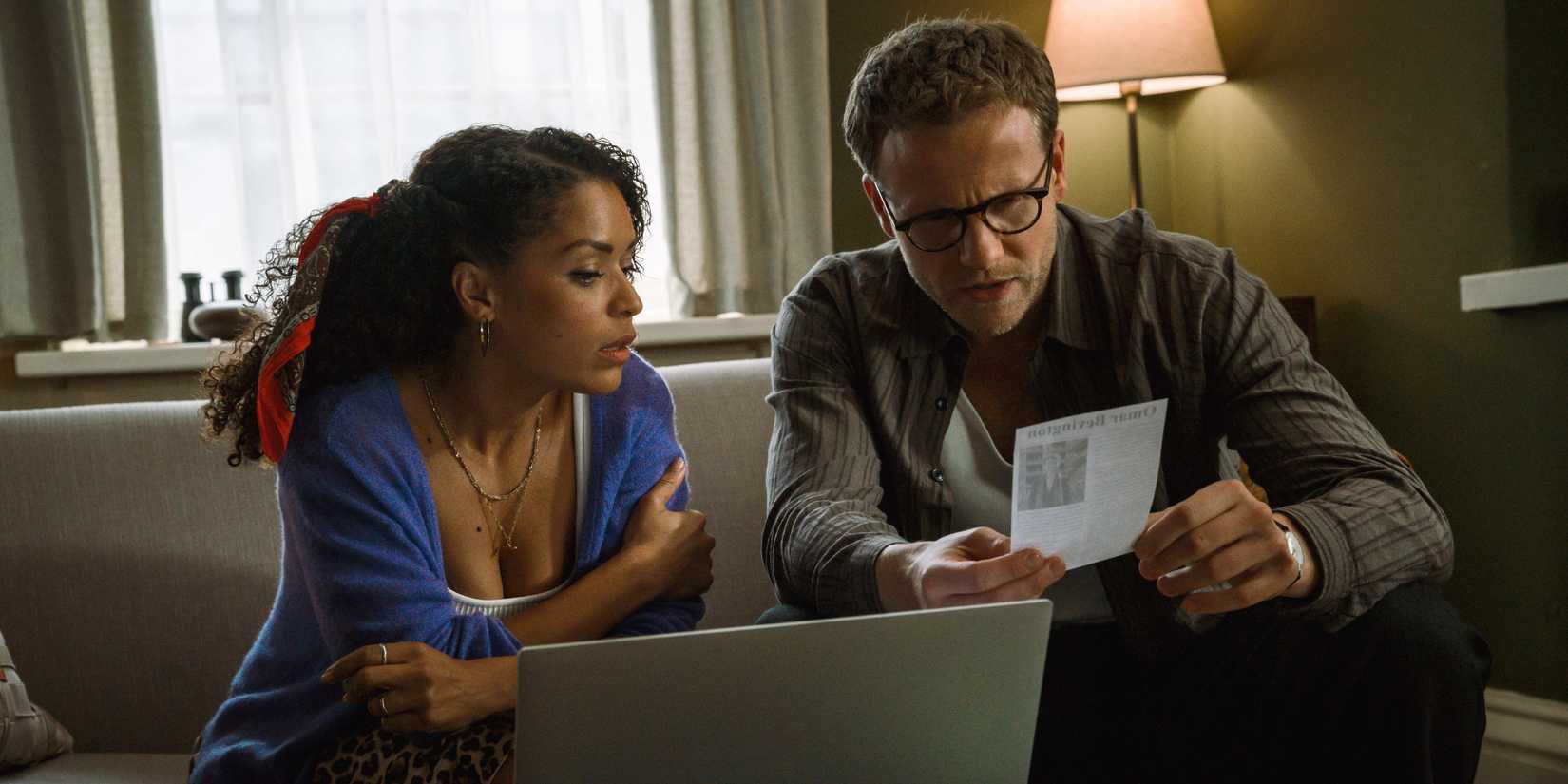 Antonia Thomas as Tuppence sitting on the couch with a laptop with Josh Dylas as Tommy in Tommy & Tuppence