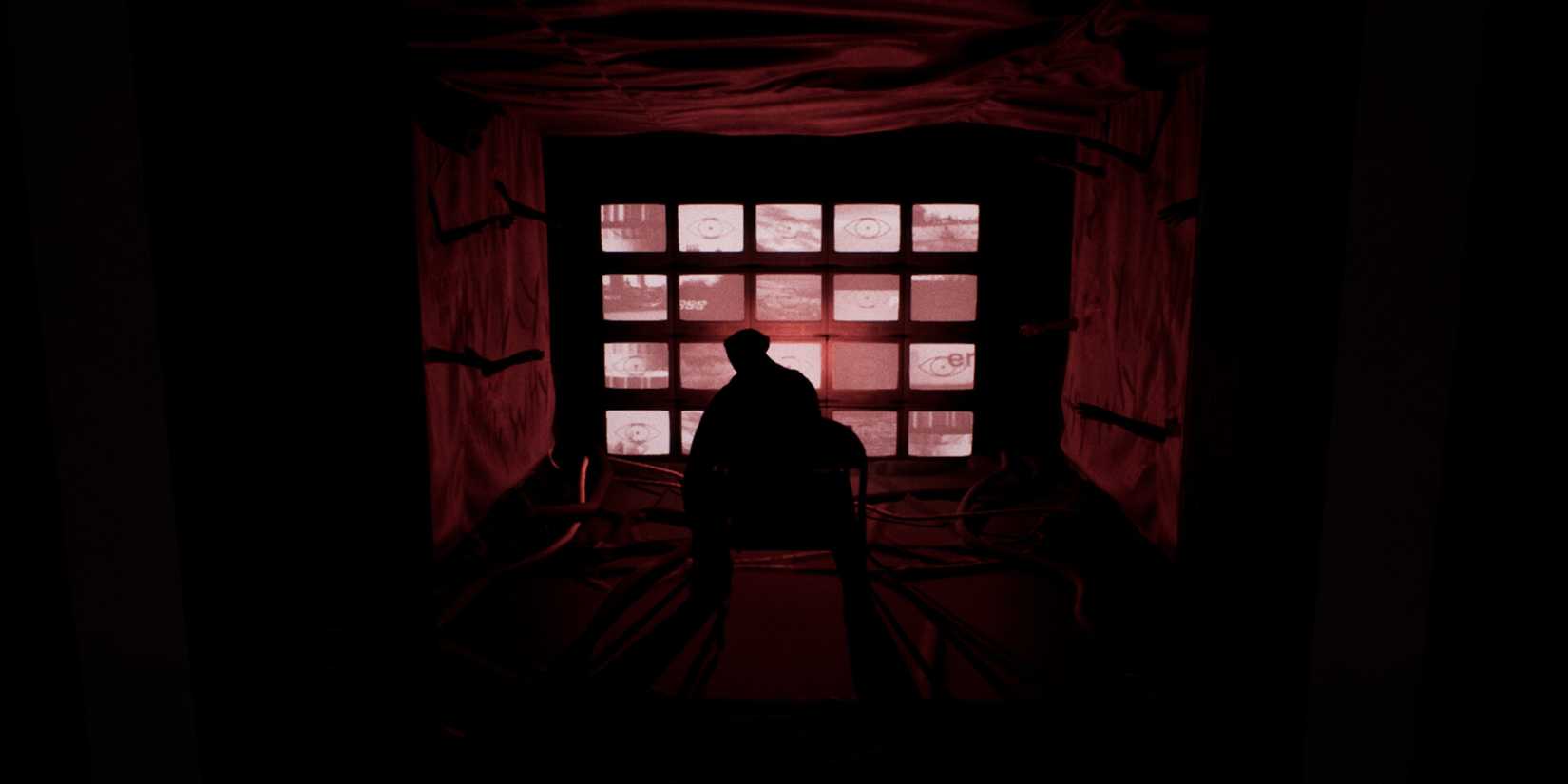 A man sitting before a wall of monitors in the game Subject